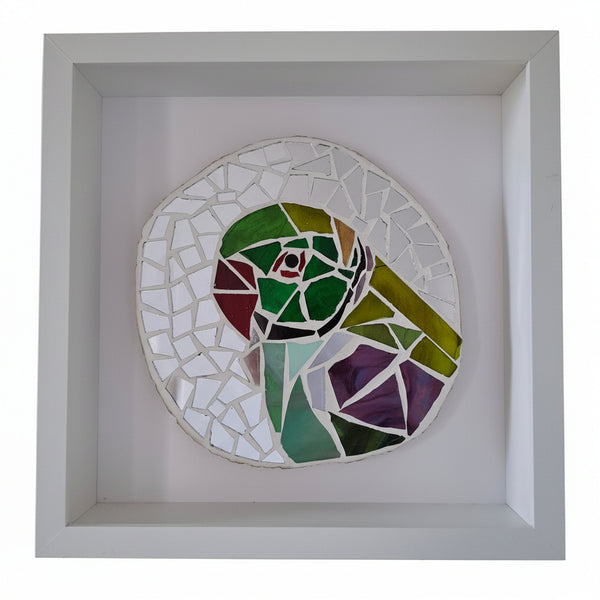 A circular mosaic wall art piece featuring a stylized parrot head in green, purple, red, and black, mounted inside a square white shadow box frame.