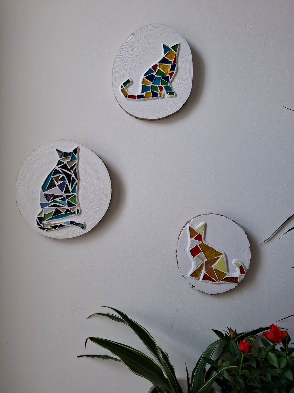 3 cat mosaics on the wall surrounded by plants 