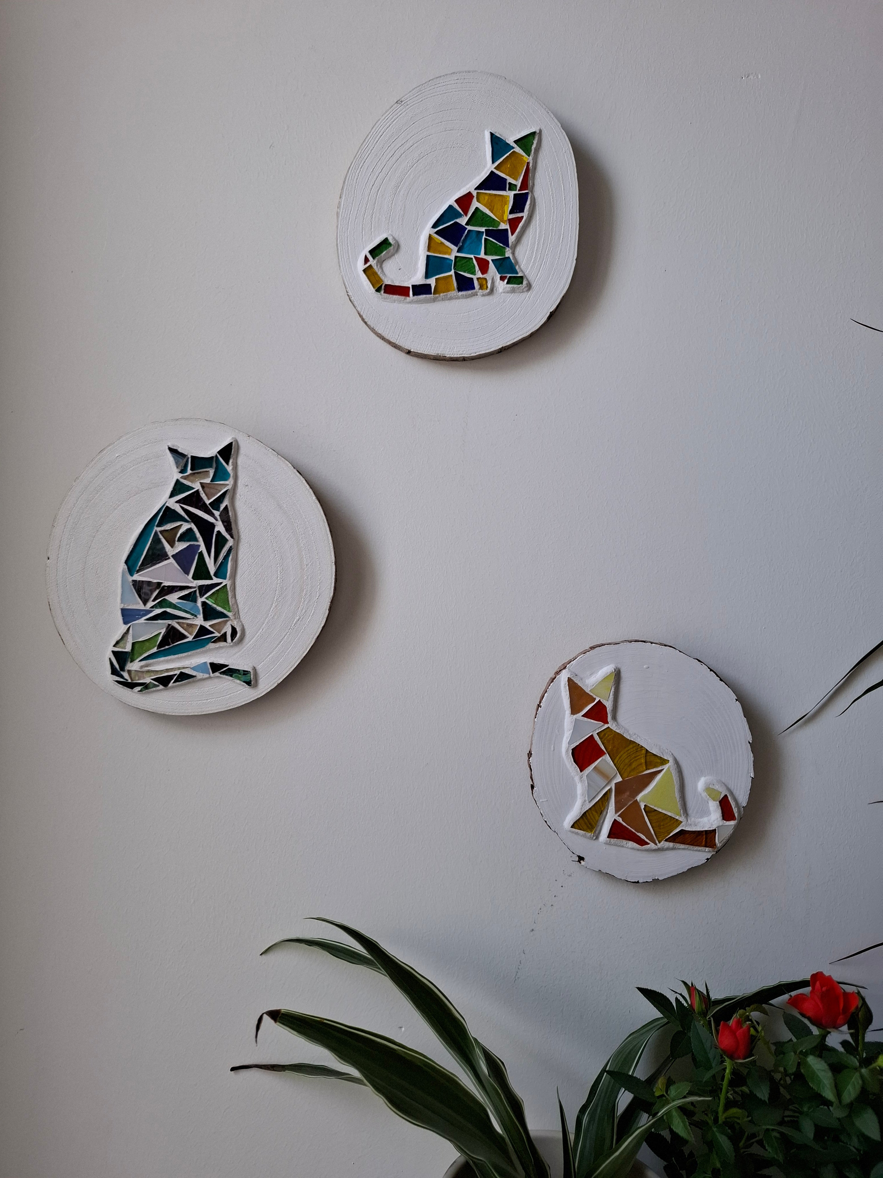 3 cat mosaics on the wall surrounded by plants 