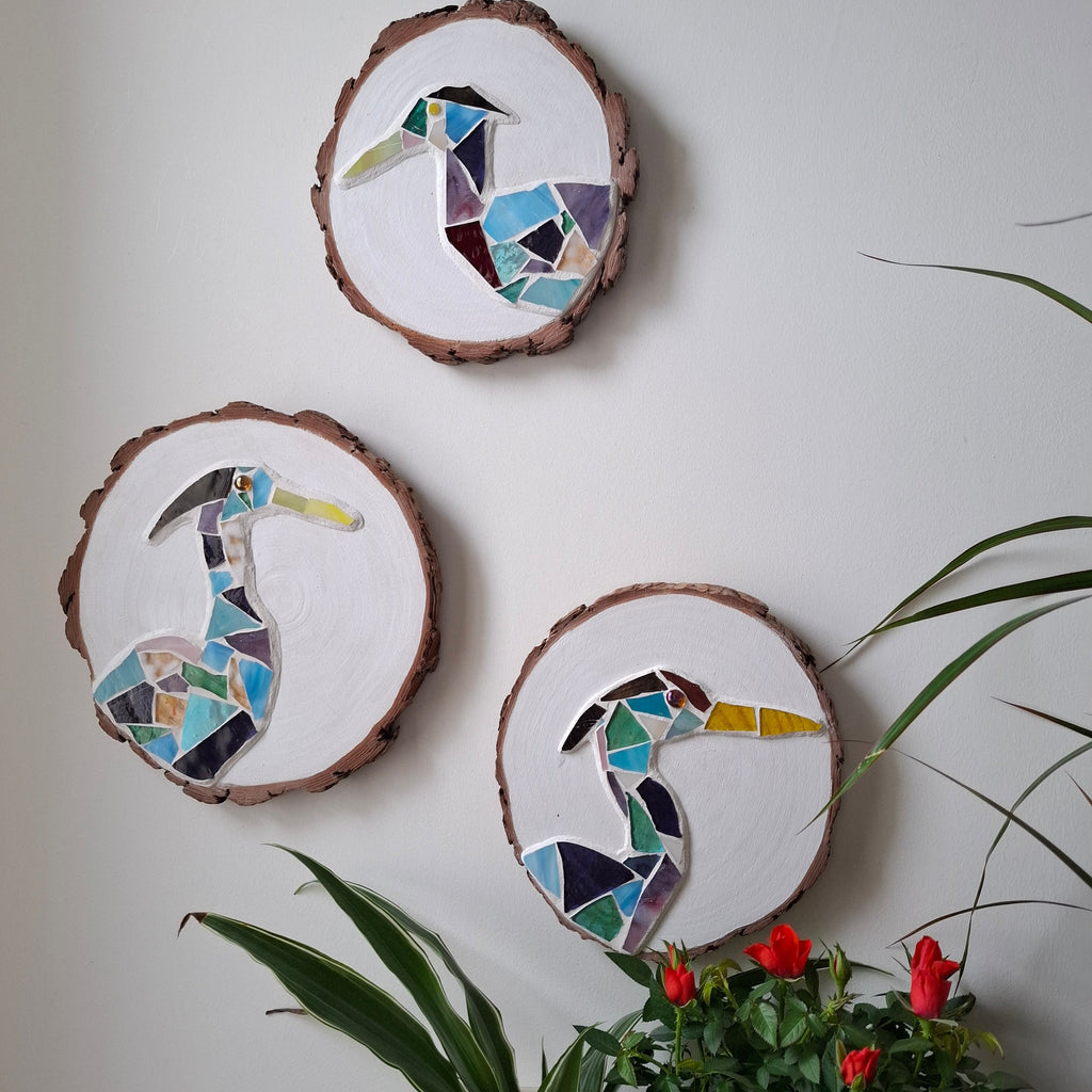 3 heron mosaics on the wall surrounded by plants 