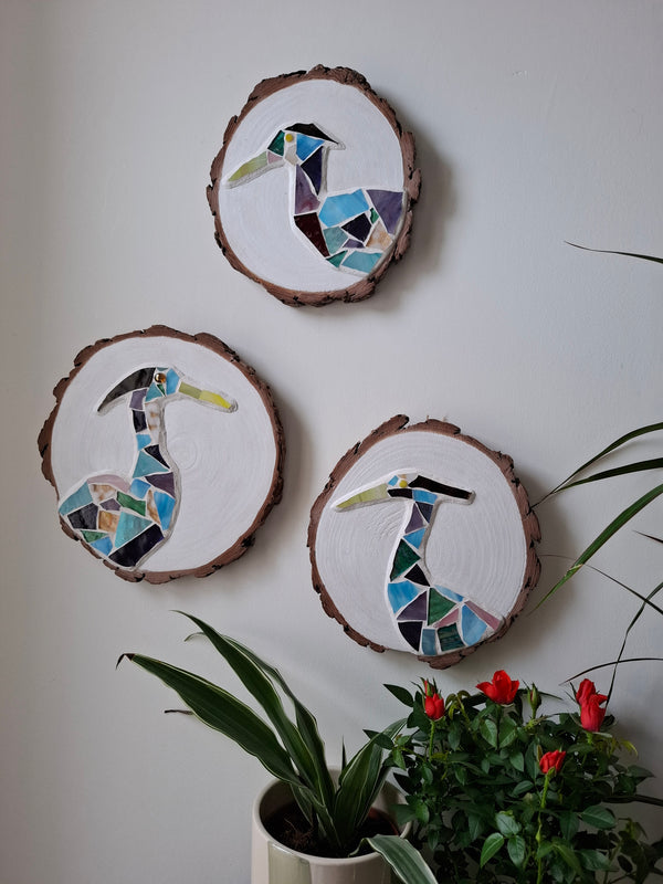 3 heron mosaics on the wall surrounded by plants 