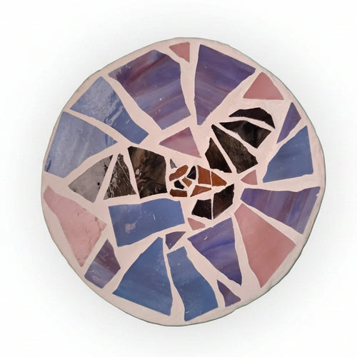 Circular mosaic wall art featuring a stylized bat design. Crafted with black and brown glass pieces on a pink and purple background, set on rustic wood.