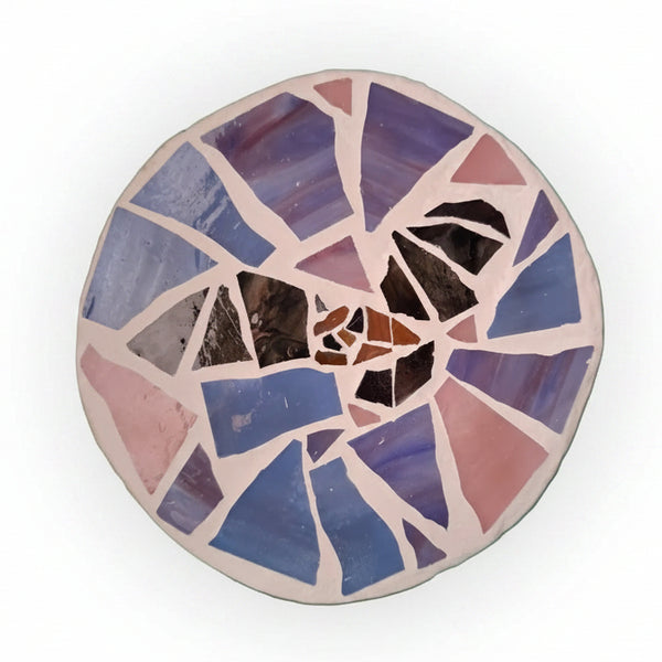 Circular mosaic wall art featuring a stylized bat design. Crafted with black and brown glass pieces on a pink and purple background, set on rustic wood.