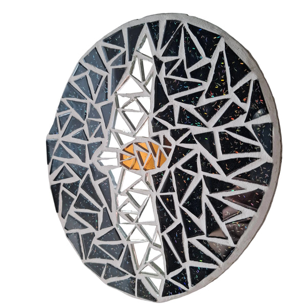 Oval mosaic wall art featuring a stylized bat design. Crafted with reflective silver and bronze glass mirror tiles on a glittery black background, set on rustic wood.