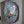 A round mosaic wall art piece mounted inside a white frame. The artwork features a yellow and black bee all set in white grout with a natural brown bark edge.