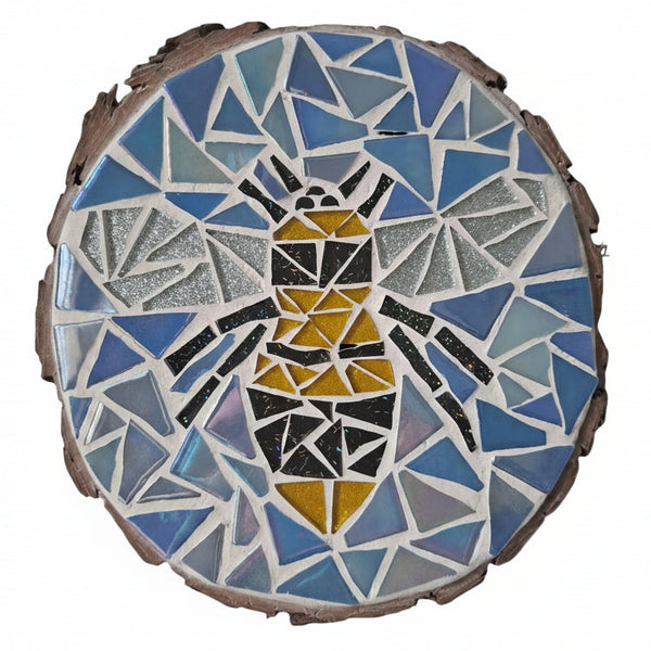 Circular mosaic wall art featuring a stylized bee design. Crafted with glittery black, gold and silver glass pieces on an iridescent blue background, set on rustic wood.