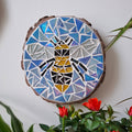 Bee mosaic on the wall surrounded by plants
