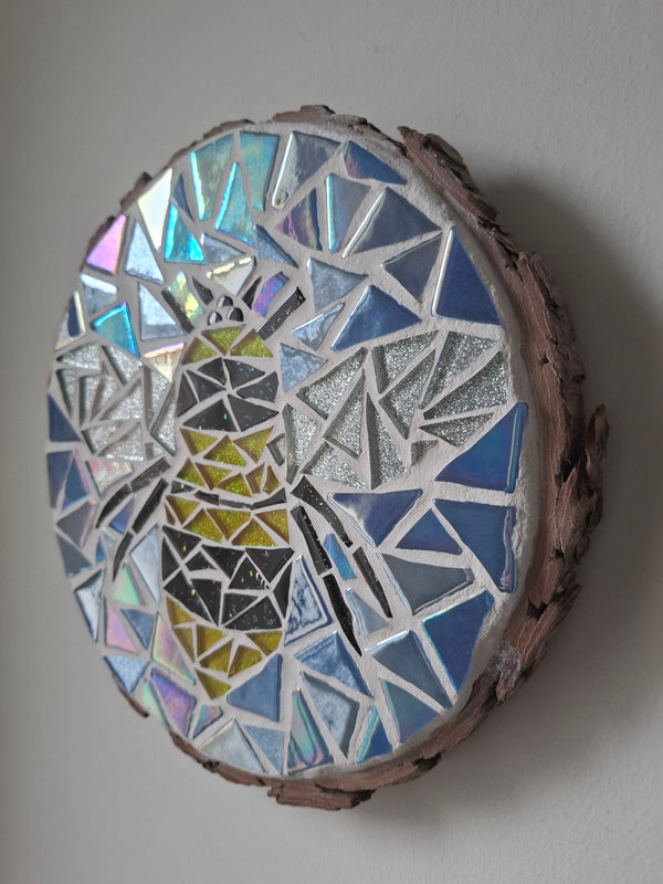 Side view of a circular bee mosaic artwork, showing the rustic wood edge.