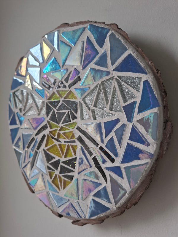 Side view of a circular bee mosaic artwork, showing the rustic wood edge.