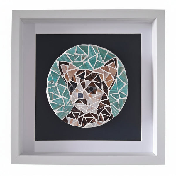 A framed mosaic art print of a dog's face, featuring geometric pieces in teal, brown, beige, and white on a dark background, housed in a white square frame.