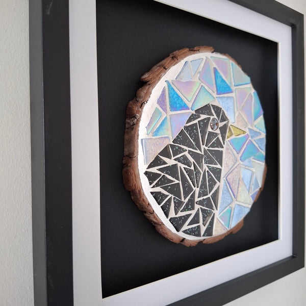 Framed mosaic bird wall art featuring a stylized bird made of black, white, and iridescent blue geometric pieces on a round natural wood slice, mounted inside a black shadowbox frame.