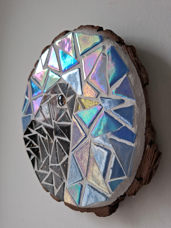 Side view of a circular bird mosaic artwork, showing the rustic wood edge.