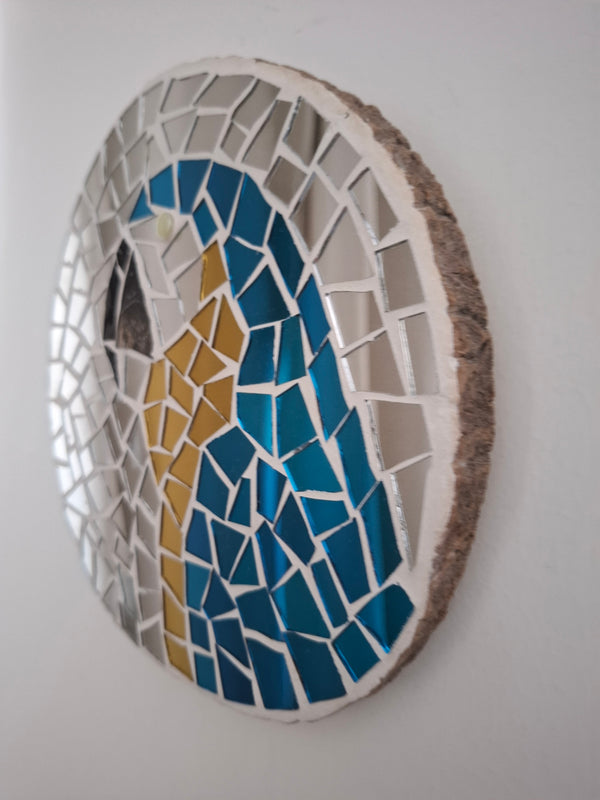 Side view of a circular macaw mosaic artwork, showing the rustic wood edge.