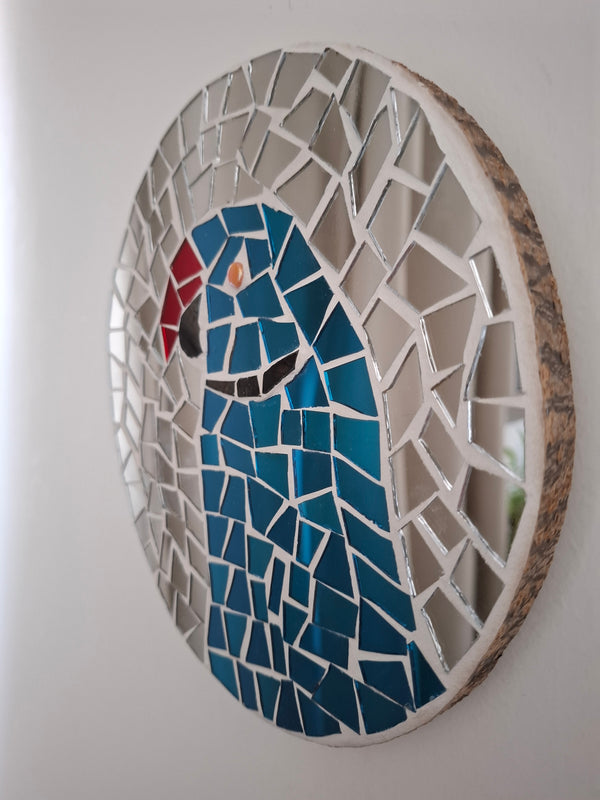 Side view of a circular parakeet mosaic artwork, showing the rustic wood edge.