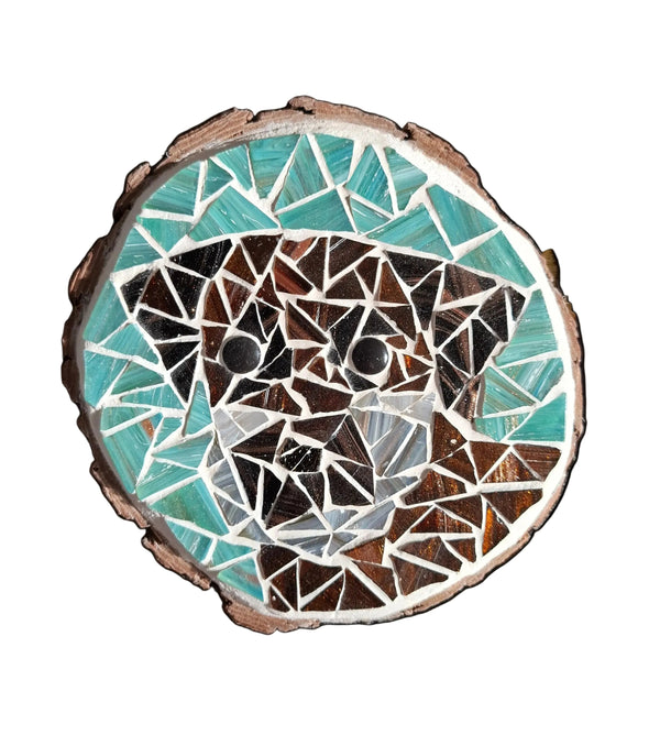 Circular mosaic wall art featuring a stylized dog design. Crafted with gold-dusted dark bronze and brown glass pieces on a gold-dusted aqua background, set on rustic wood.