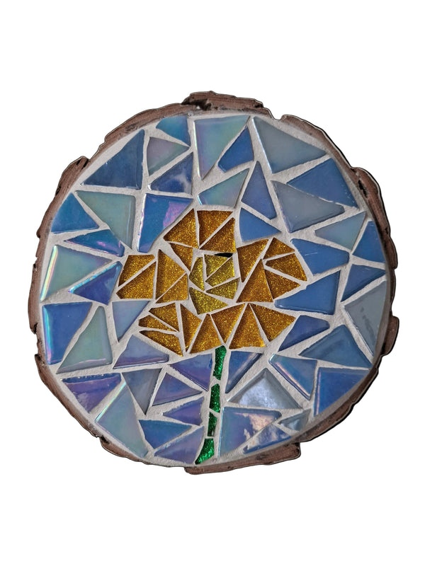 Circular mosaic wall art featuring a stylized flower design. Crafted with glittery gold and yellow glass pieces on an iridescent blue background, set on rustic wood.