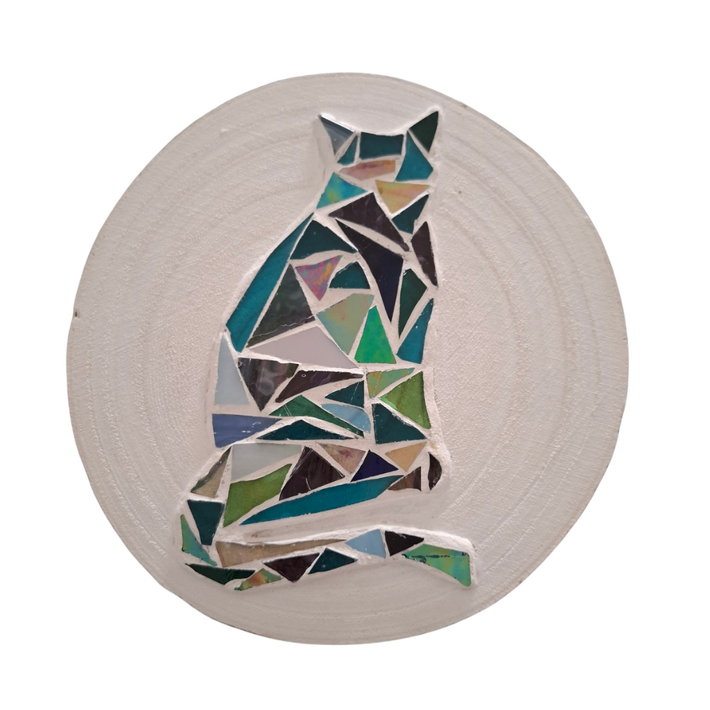 Circular mosaic wall art featuring a stylized cat silhouette design. Crafted with blue, green and aqua stained glass pieces on a striking white painted background, set on rustic wood.
