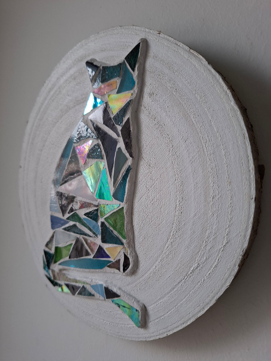 Side view of a circular cat silhouette mosaic artwork, showing the rustic wood edge.