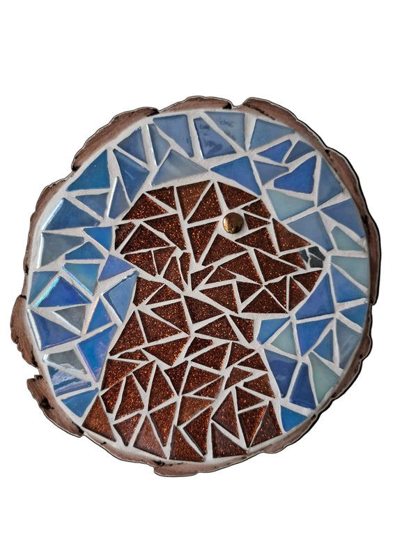 Circular mosaic wall art featuring a stylized dog design. Crafted with glittery brown glass pieces on an iridescent blue background, set on rustic wood.