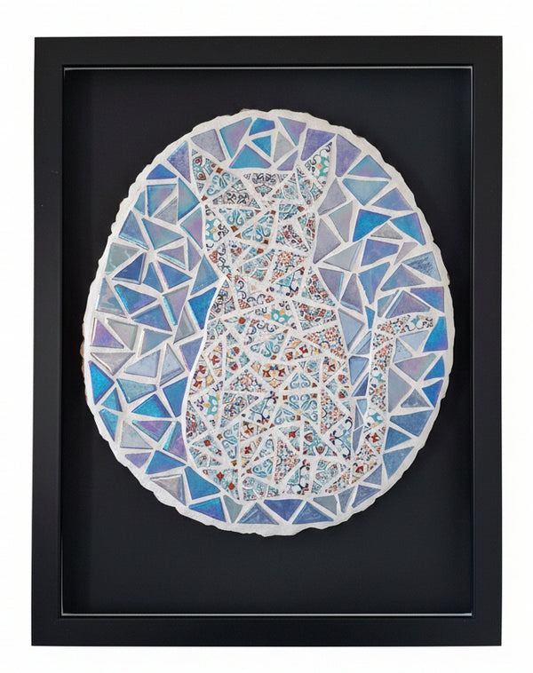 A framed mosaic art print depicting a cat in a circular frame, featuring blue, purple, and red patterned triangles on a black background, mounted on a light gray wall.