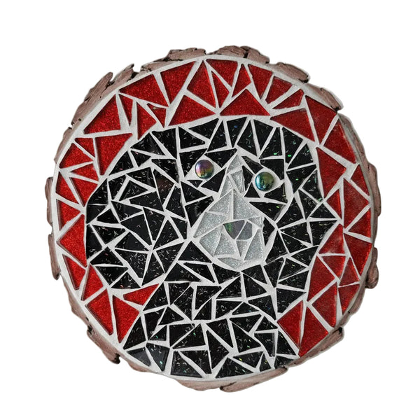 Circular mosaic wall art featuring a stylized dog design. Crafted with glittery black and white glass pieces on an glittery red background, set on rustic wood.