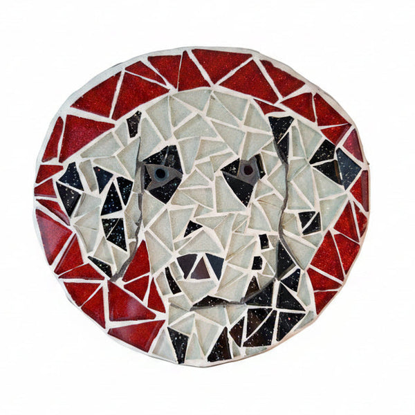 Circular mosaic wall art featuring a stylized dog design. Crafted with glittery black and white glass pieces on a sparkly red background, set on rustic wood.