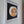 A framed circular mosaic wall art piece featuring a stylized dog face made of mirror tiles in bronze, brown, and white, mounted on a black background inside a white frame.
