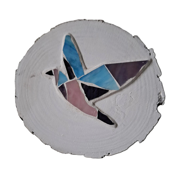 Circular mosaic wall art featuring a stylized dove design. Crafted with pink, purple and blue stained glass pieces on a painted white background, set on rustic wood.
