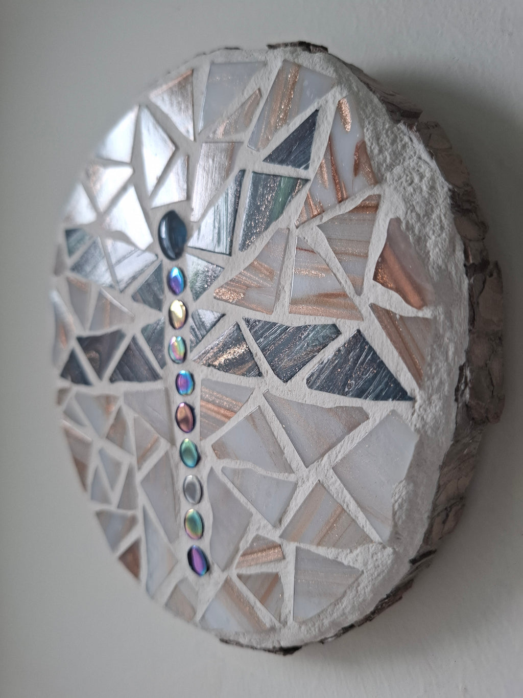 Side view of a circular dragonfly mosaic artwork, showing the rustic wood edge.