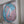 A circular mosaic wall art piece featuring a stylized flamingo, constructed with light blue and pink glitter tiles and white grout, mounted inside a white recessed shelf.
