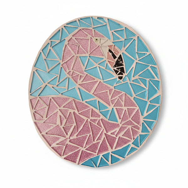 Circular mosaic wall art featuring a stylized flamingo design. Crafted with glittery pink glass pieces on a sparkly blue background, set on rustic wood.