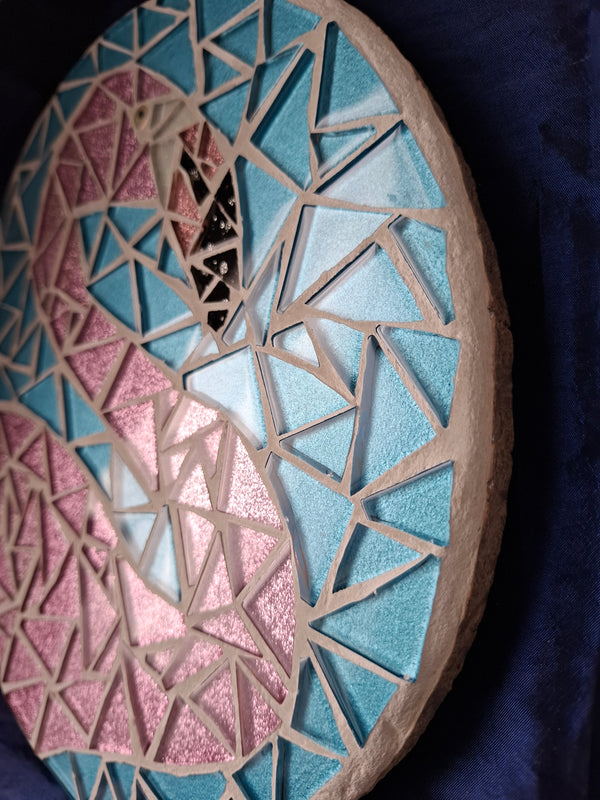 Side view of a circular flamingo mosaic artwork, showing the rustic wood edge.