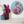 A round mosaic wall art piece featuring a flamingo design in red, cream, and light blue, displayed on a white wall above a shelf with decorative vases and flowers.