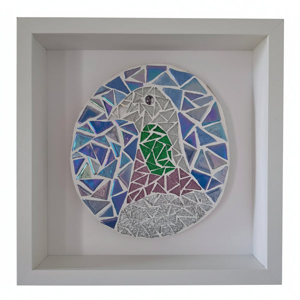 A circular stained glass art piece depicting a stylized bird, mounted inside a square white shadow box display. The bird design features blue, purple, green, and silver mosaic glass panels.