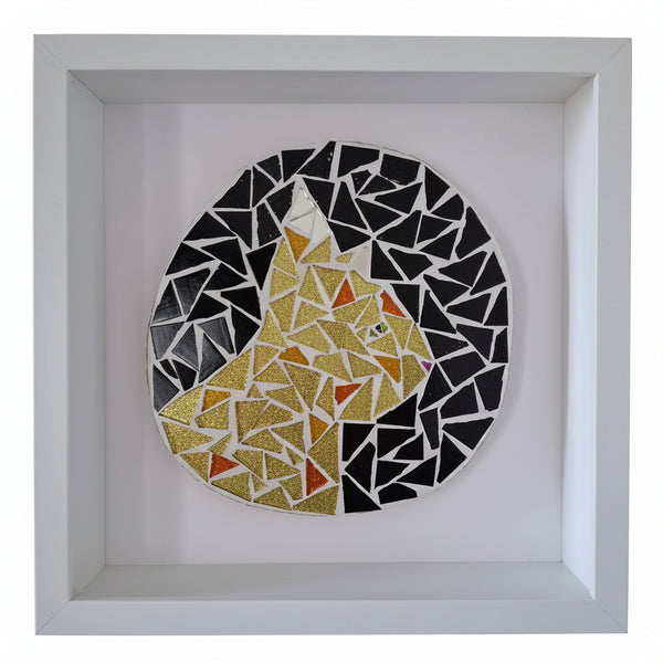 A circular mosaic wall art piece depicting a cat, mounted in a square white shadow box frame. The cat is composed of gold glitter and orange mosaic tiles, surrounded by a black and white geometric pattern.