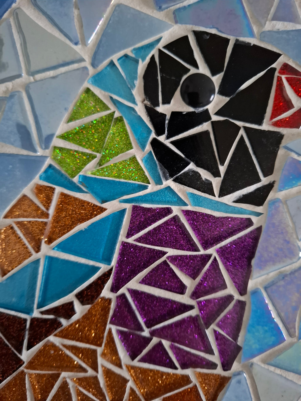 Close up of a circular bird mosaic artwork, showing the rustic wood edge.