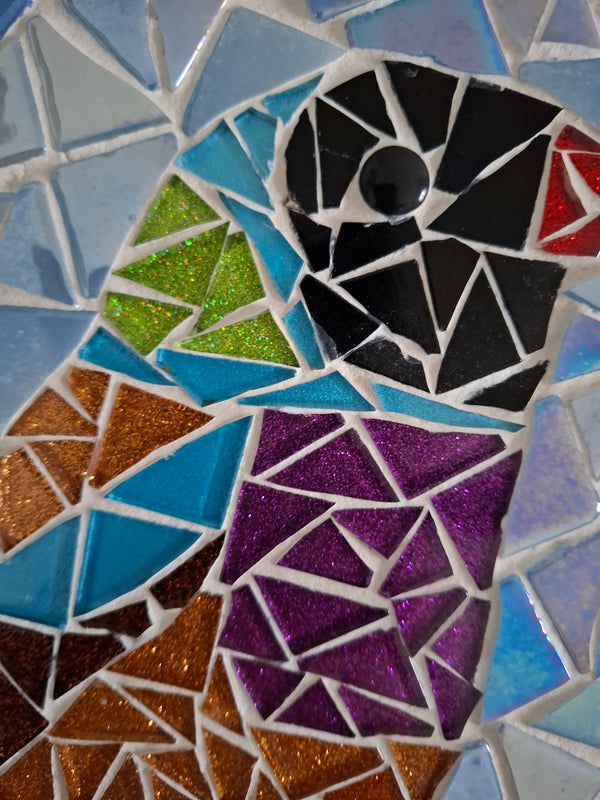 Close up of a circular bird mosaic artwork, showing the rustic wood edge.