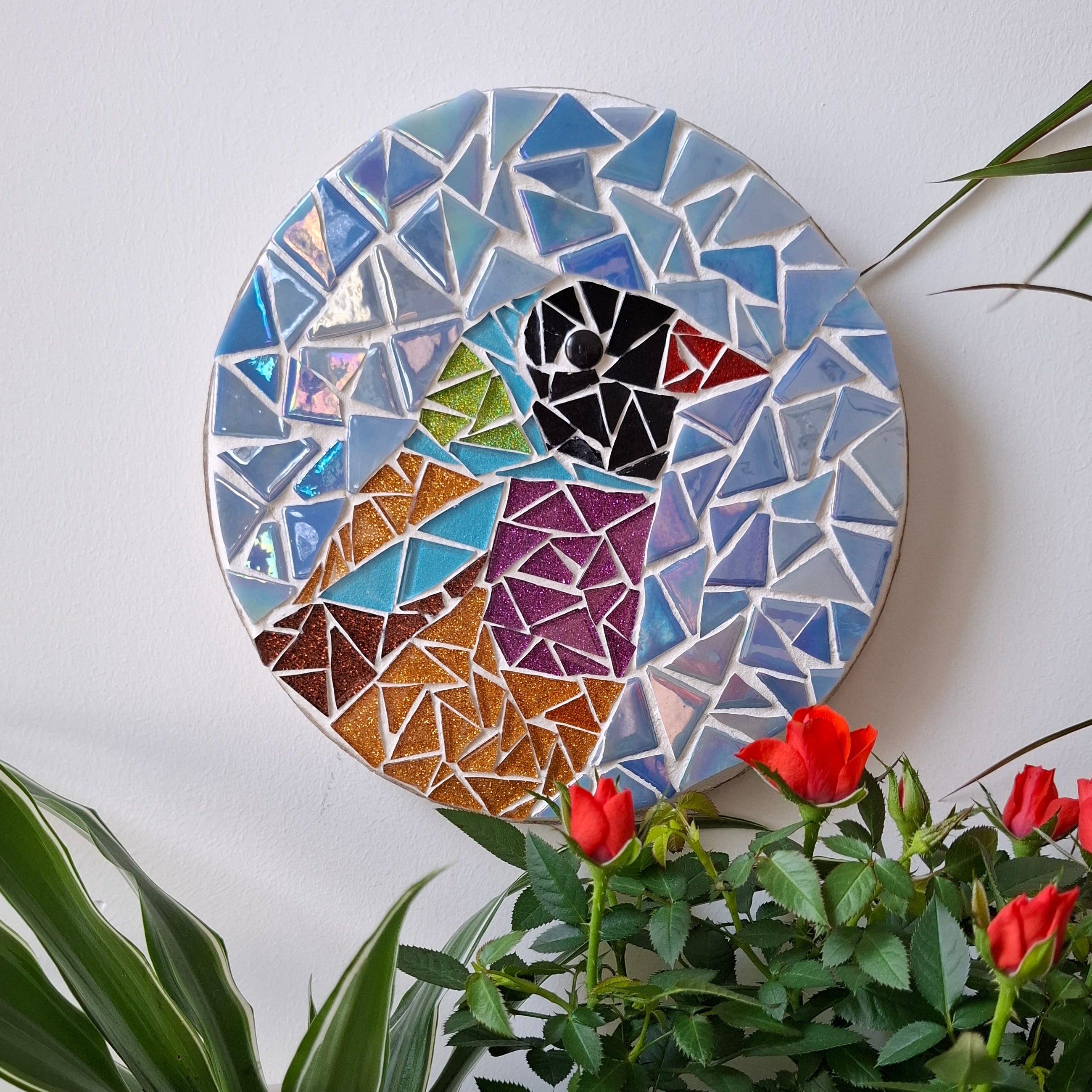 Bird mosaic on the wall surrounded by plants
