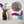 A styled interior shelf scene with dried flowers in an amber glass bottle and a blue ceramic pot, next to a round mosaic wall hanging featuring a great tit bird.