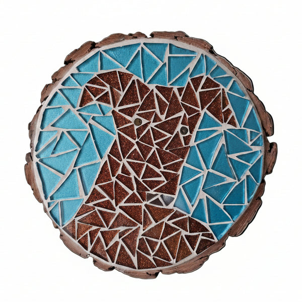Circular mosaic wall art featuring a stylized dog design. Crafted with glittery brown glass pieces on a sparkly blue background, set on rustic wood.