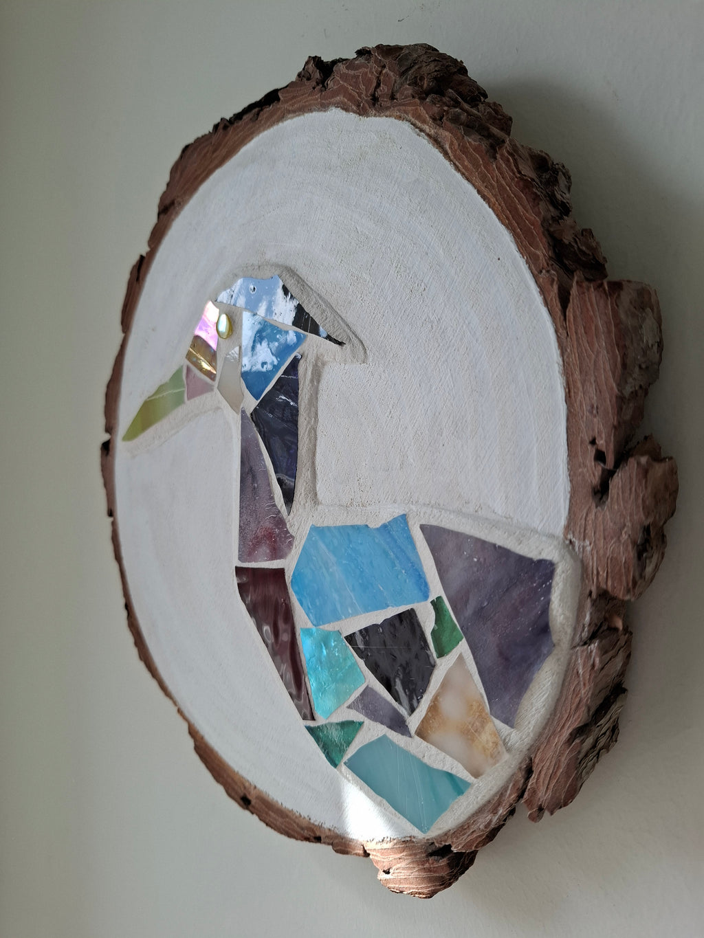 Side view of a circular heron mosaic artwork, showing the rustic wood edge.