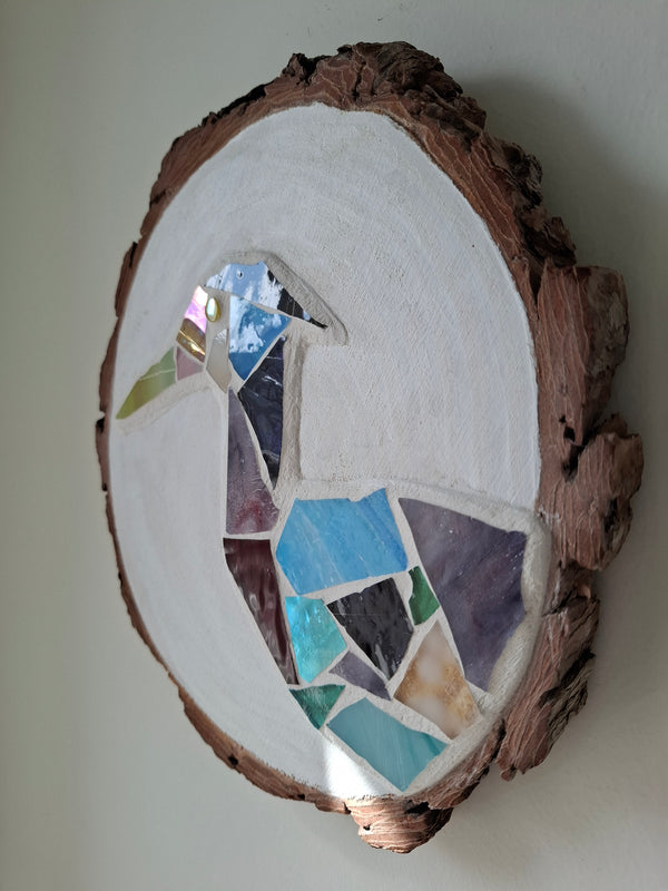 Side view of a circular heron mosaic artwork, showing the rustic wood edge.