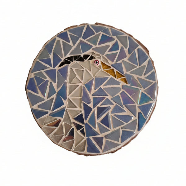 Circular mosaic wall art featuring a stylized heron design. Crafted with glittery white and silver mirror glass pieces on an iridescent blue background, set on rustic wood.