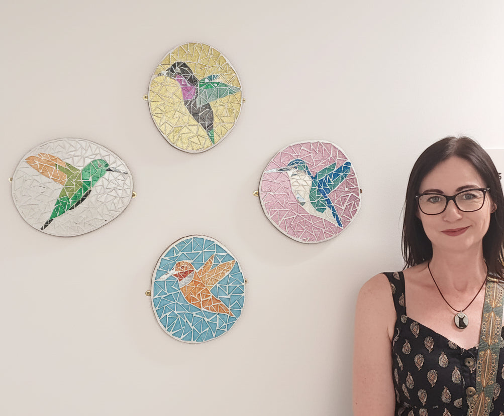 Naomi Hope, mosaic artist, standing next to her exhibition of colourful hummingbird mosaics at the Royal Derby Hospital 