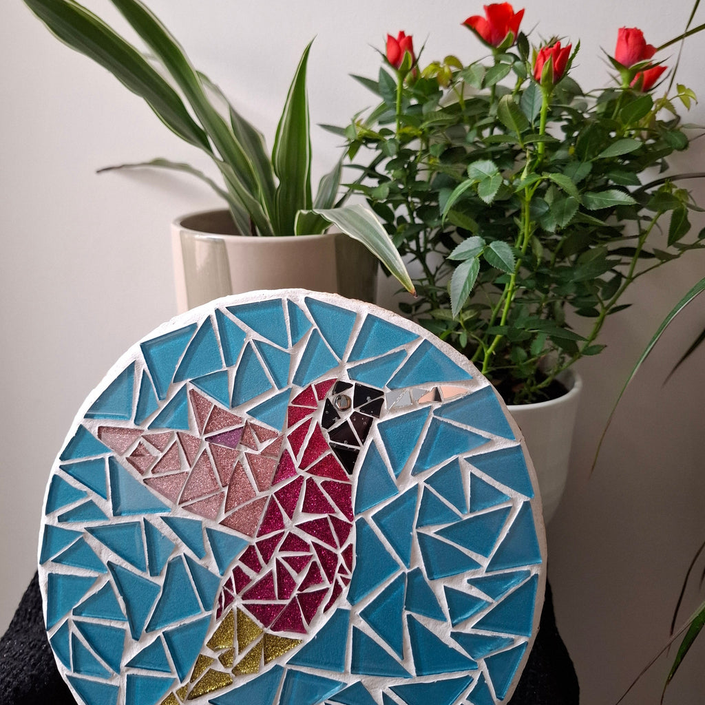 Bird mosaic on the wall surrounded by plants
