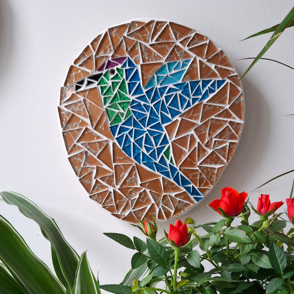 Bird mosaic on the wall surrounded by plants
