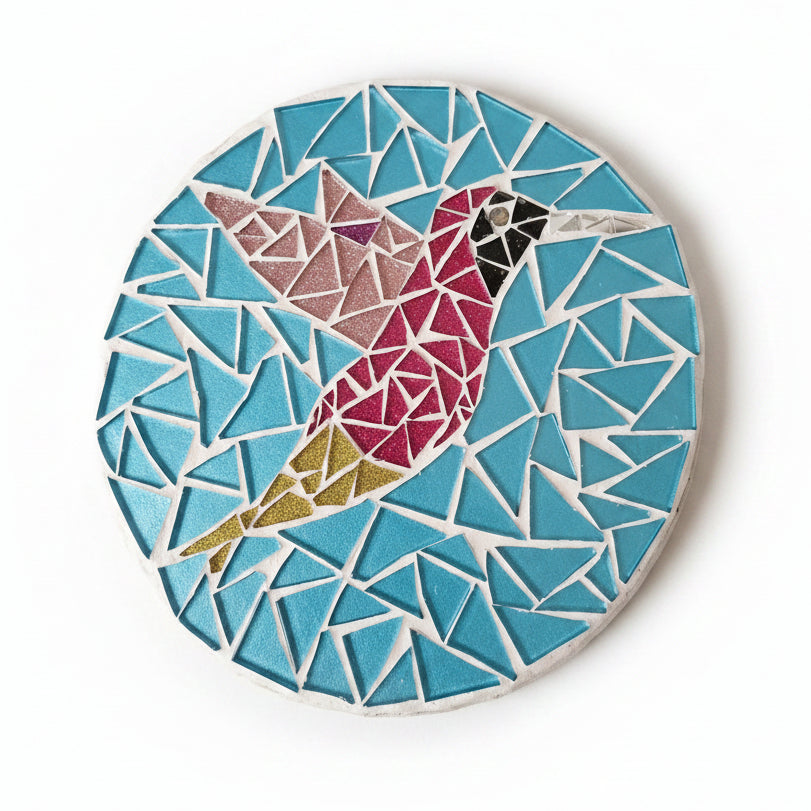 Circular mosaic wall art featuring a stylized hummingbird design. Crafted with glittery pink and gold glass pieces on a sparkly blue background, set on rustic wood.