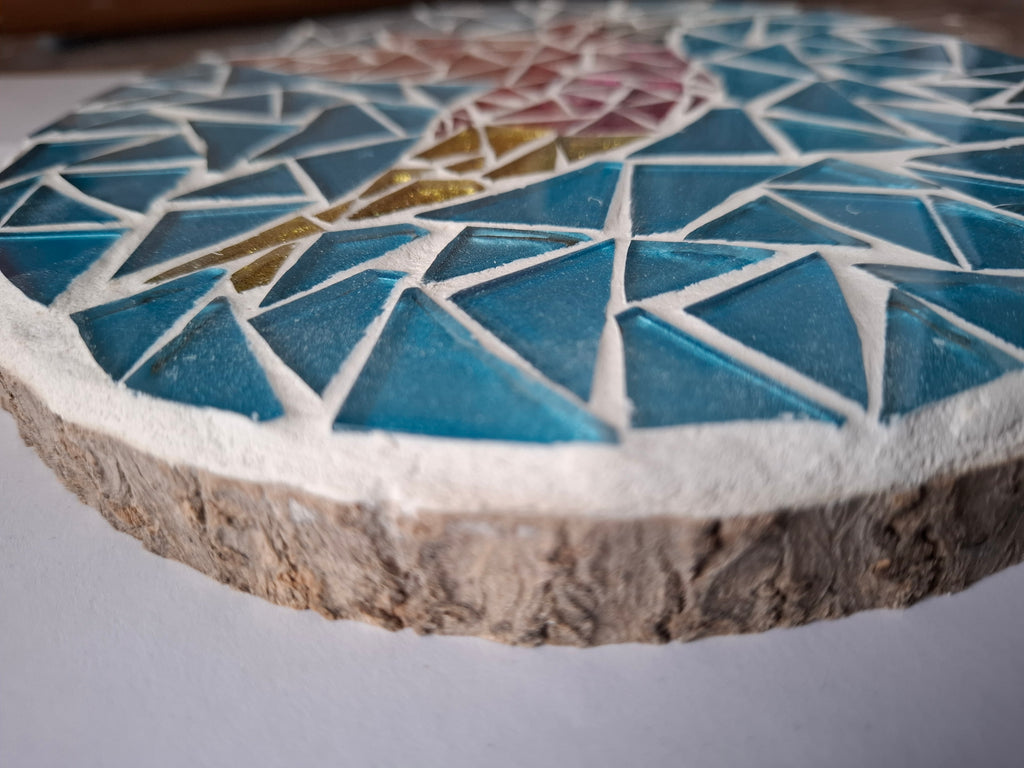 Side view of a circular bird mosaic artwork, showing the rustic wood edge.