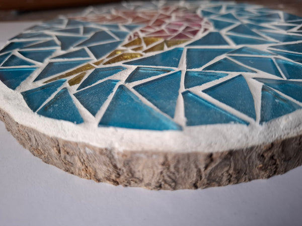 Side view of a circular bird mosaic artwork, showing the rustic wood edge.