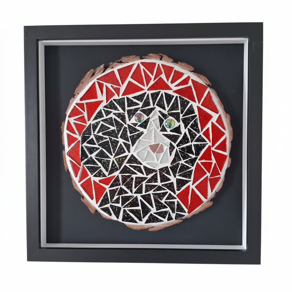 A framed mosaic art piece depicting a stylized dog face, mounted on a black backing and enclosed in a black shadow box frame, shown hanging on a light wall.